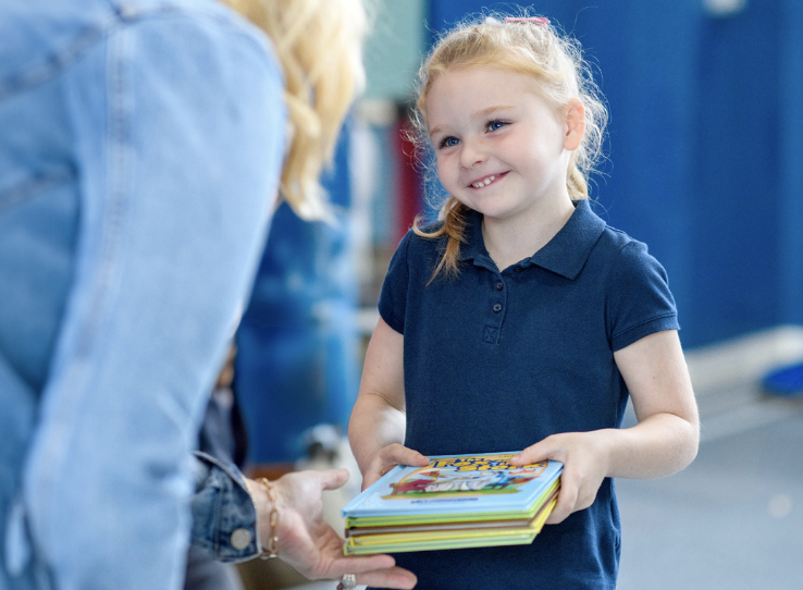 Young girl holding books to check out from her community library. 